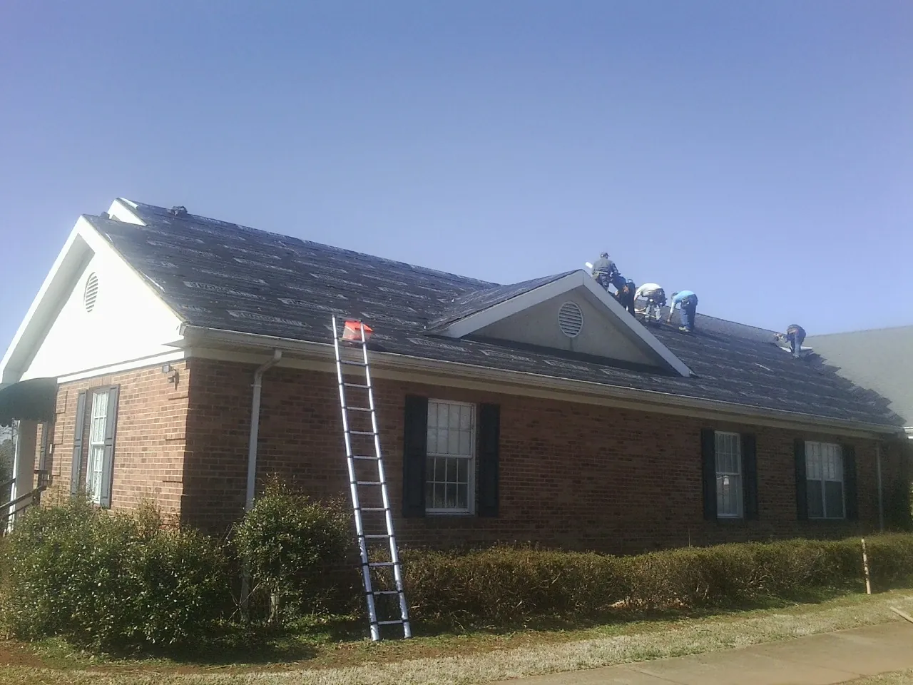 Crew tearing shingles off a brick ranch roof with a ladder set — Metal Roof Repair work by our crew in Cassoday