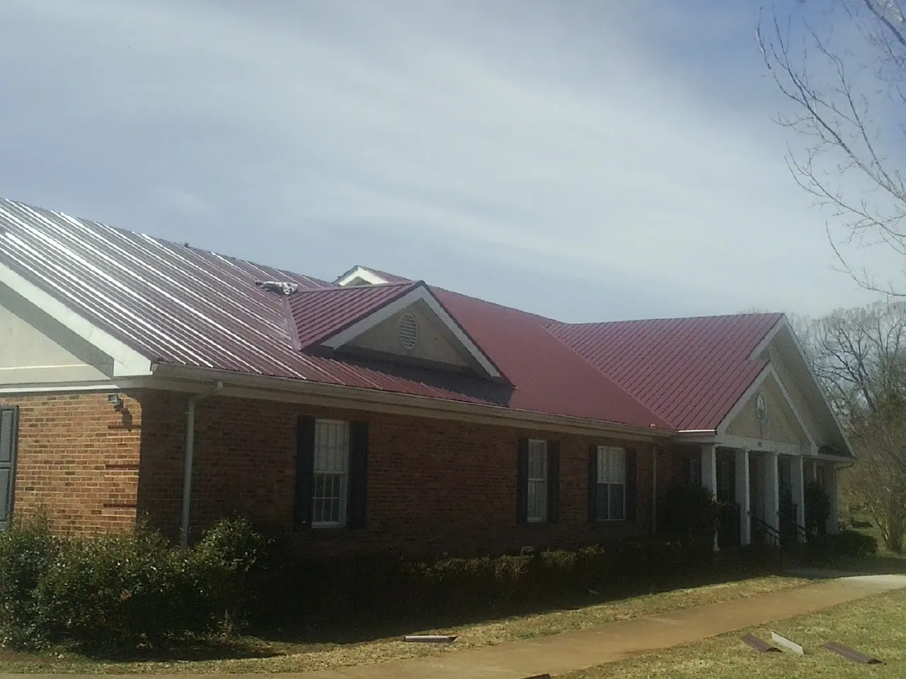 Red metal roof with gabled entries on a long brick building, from a Hail Damage Roof Repair job in Cassoday