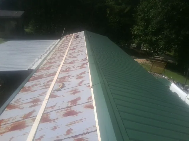 Old rusted panels beside newly installed green metal roofing — Wind Damage Roof Repair by Roofing Brothers in Cassoday