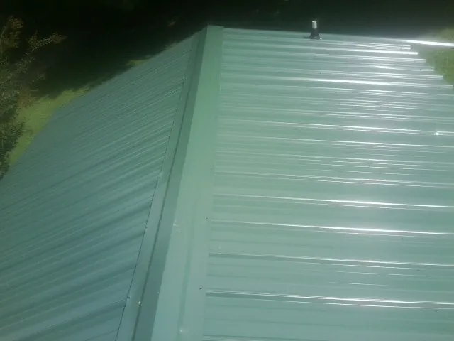 New green metal panels meeting at the ridge of a roof — Flat Roof Repair work by our crew in Cassoday