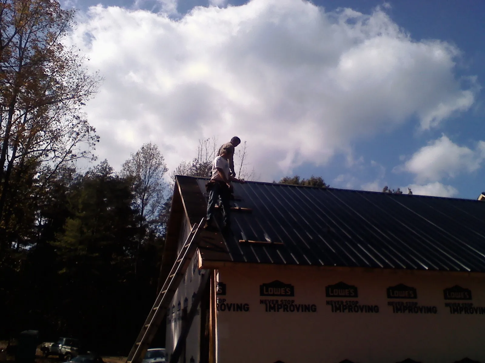 Roofer fastening dark metal panels high against a cloudy sky, from a Roof Inspection job in Cassoday