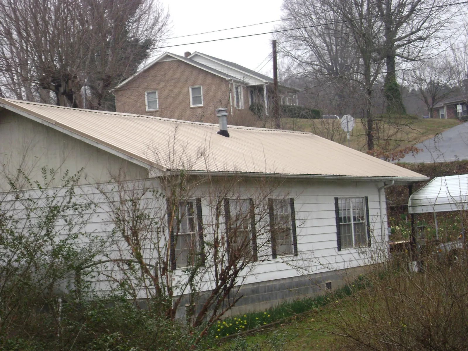 Tan metal roof on a white sided house set into a hillside — Commercial Roofing by Roofing Brothers in Cassoday